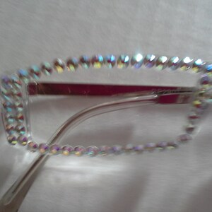 May include: Clear plastic frame glasses with a row of iridescent rhinestones around the edge.