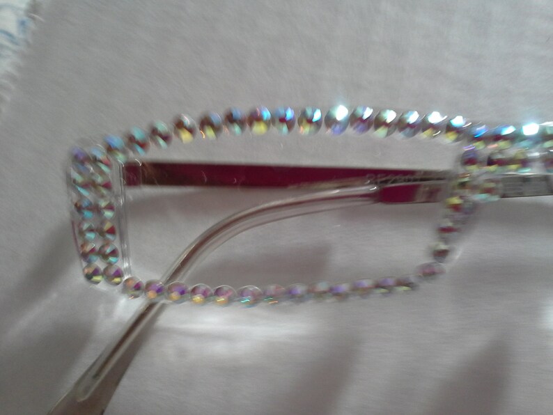 May include: Clear plastic frame glasses with a row of iridescent rhinestones around the edge.