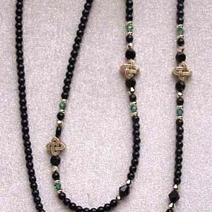May include: Black and green beaded eyeglass chain with gold accents. The chain features four gold Celtic knot charms.