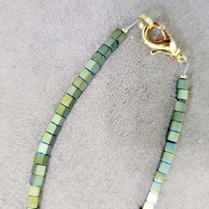 May include: A green and gold beaded necklace with a gold clasp.