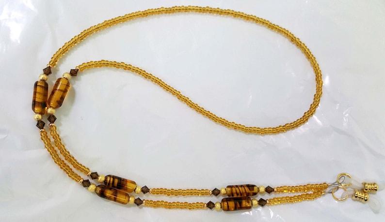 May include: A gold beaded eyeglass chain with brown and gold striped beads and clear crystal accents.