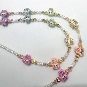 May include: A close-up of three beaded necklaces with bunny-shaped charms. The charms are in various pastel colors, including pink, purple, green, and yellow. The beads are gold, white, and clear. The necklaces are on a white background.