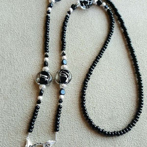 May include: A black beaded lanyard with silver accents and decorative glass beads. The lanyard features a large silver ring at the bottom for holding keys or an ID badge. The glass beads have a black and white design.
