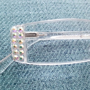 May include: Clear plastic rectangular frame glasses with a row of iridescent rhinestones on the side.