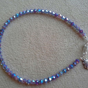 May include: A delicate anklet made with iridescent blue and purple crystal beads. The anklet has a silver clasp and a small seashell charm.