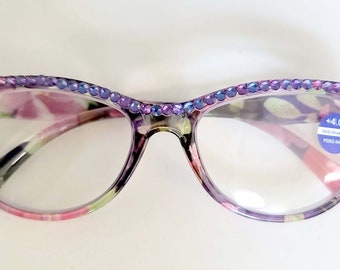 May include: Floral print reading glasses with a purple and blue rhinestone trim. The glasses have a +4.00 lens and anti-blue light protection.