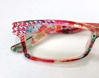 May include: Floral print reading glasses with a clear lens and a row of pink rhinestones on the top of the frame.