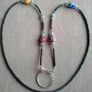 May include: A black beaded lanyard with a silver retractable badge holder and colorful flower-shaped beads. The lanyard has turquoise and silver beads.