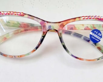 May include: Floral patterned reading glasses with pink rhinestones on the top rim. The glasses have a +1.50 magnification.