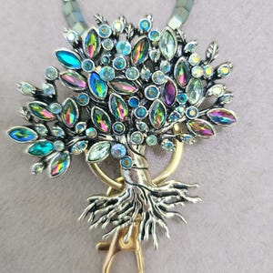 May include: A silver and gold tree of life keychain with iridescent blue, green, and purple crystals. The keychain has a gold clasp.
