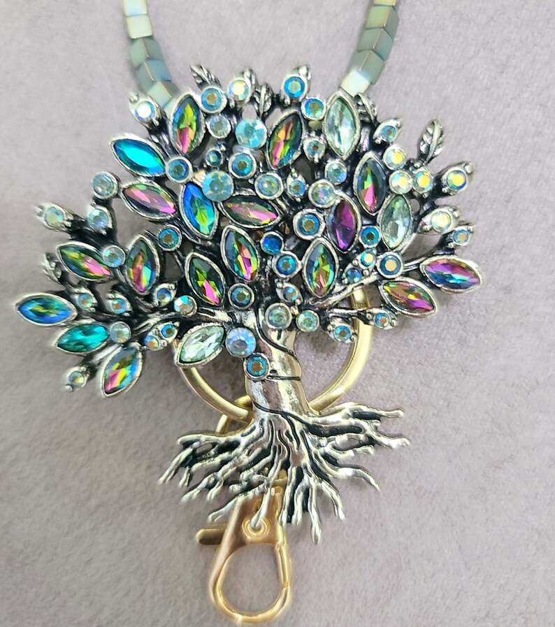 May include: A silver and gold tree of life keychain with iridescent blue, green, and purple crystals. The keychain has a gold clasp.