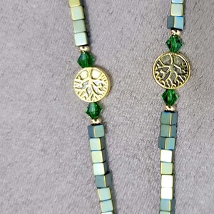 May include: A green and silver beaded necklace with gold tree of life charms and green crystal accents.