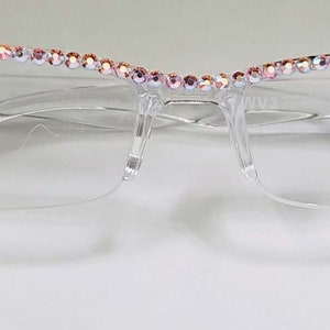May include: Clear plastic frame glasses with a row of iridescent rhinestones around the top edge.