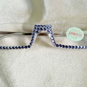 May include: Clear plastic frame glasses with a blue rhinestone trim. The glasses have a square shape with rounded corners. The label on the glasses reads "HANDEMED LOCATED LENS APPROVED ASIAN SIZE MADE IN TAIWAN".