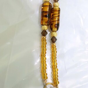 May include: A pair of gold-toned eyeglass chains with clear plastic ends and brown and gold beads. The chains are made of small, round beads.