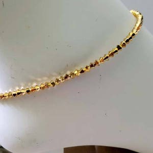 May include: A gold anklet with small, faceted beads. The anklet is on a white mannequin leg.