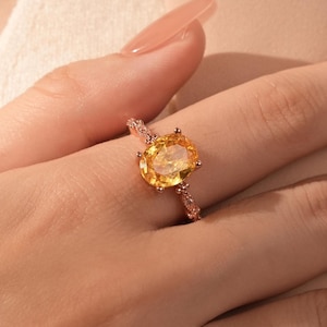 Peut inclure: Une bague en or avec une grande pierre précieuse jaune de forme ovale entourée de petites pierres précieuses claires.