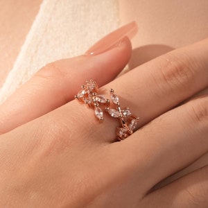 May include: A rose gold ring featuring a delicate design of leaves and clear cubic zirconia stones.