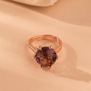 May include: Rose gold ring featuring a large, round, faceted, smoky quartz gemstone. The ring has a delicate band with small accent stones. The gemstone is a deep brown color, and the ring is set against a neutral background.