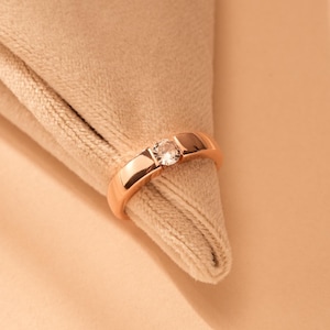 May include: A rose gold ring with a single clear gemstone set in the centre.