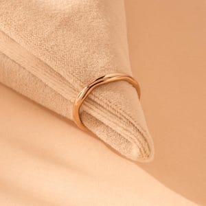 Può includere: Un anello in oro rosa lucido con una fascia liscia e arrotondata. La superficie metallica è riflettente e presenta un design circolare continuo. L'anello è ripreso in una vista chiara e nitida, che mette in risalto la lucentezza del metallo.