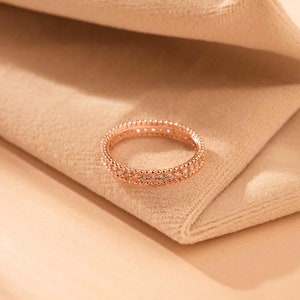 Könnte beinhalten: Ein Ring aus Roségold mit einem zarten Perlenmuster und kleinen klaren Steinen.