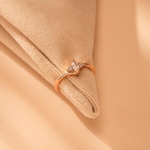 May include: A delicate rose gold ring featuring a marquise-shaped clear stone and two smaller round stones on the band.