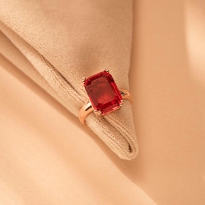 Puede incluir: Un anillo de oro rosa con una gran piedra preciosa roja de talla esmeralda.