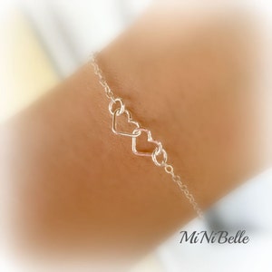 May include: A silver chain bracelet with three interlocking heart charms. The bracelet is on a person's wrist.