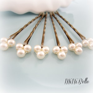 May include: Set of six silver hair pins with three white pearl beads on each pin. The pins are arranged in a fan shape on a light blue surface.