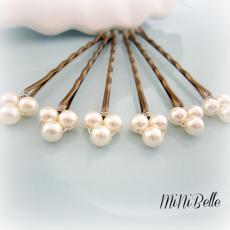 May include: Set of six silver hair pins with three white pearl beads on each pin. The pins are arranged in a fan shape on a light blue surface.