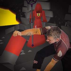 May include: A person wearing a red and brown rash guard and black pants is holding a red fabric. In the background, a red hooded figure stands on a pedestal with a black staff.