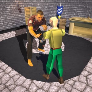 May include: A man in a red and black shirt is demonstrating a martial arts move to a green and yellow figure. The figure is standing on a black mat in a room with brick walls.