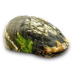 Puede incluir: Gorra plana de camuflaje con un estampado de hojas en tonos verdes, marrones y beige. El sombrero tiene una corona redondeada y una visera peque&ntilde;a y r&iacute;gida. La tela tiene un aspecto texturizado.