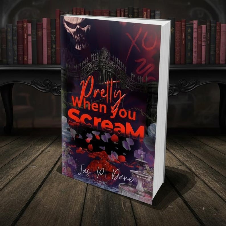 May include: A book titled Pretty When You Scream by Jas P. Dane. The cover features a dark, gothic illustration with a skull, an ornate iron gate, a fountain, and red rose petals. The title is written in bold red and orange lettering.