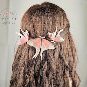 May include: Three delicate pink and white butterfly hair clips, crafted to bloom, are pinned into a woman's long brown hair. The hair clips are made of delicate, translucent material and feature intricate wing details.