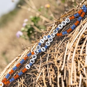 May include: A beaded bracelet featuring alternating blue and orange faceted beads with white letter beads spelling out the phrase I KNEW IT I KNEW YOU. The bracelet is constructed with a repeating pattern of small, colorful, textured beads.