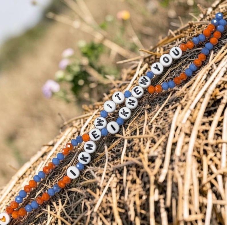 May include: A beaded bracelet featuring alternating blue and orange faceted beads with white letter beads spelling out the phrase I KNEW IT I KNEW YOU. The bracelet is constructed with a repeating pattern of small, colorful, textured beads.