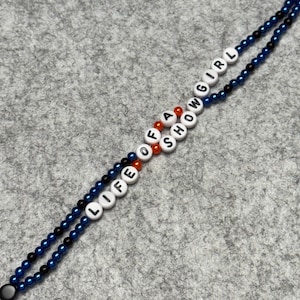 Bracelet made of 2 intertwining strings of 4mm dia dark blue and black beads with white beads with black letters that say "LIFE OF A SHOWGIRL"