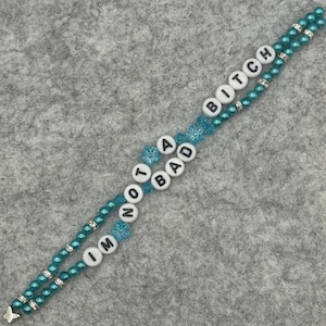 May include: A beaded bracelet with the text "I'M NOT A BAD BITCH" in white letter beads. The bracelet is turquoise with silver accents and a small butterfly charm.