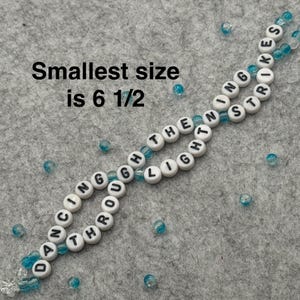 A handmade bracelet with white letter beads spelling "DANCING THROUGH THE LIGHT STRIKES". The smallest size is 6 1/2 inches. The bracelet is strung with clear and blue beads.