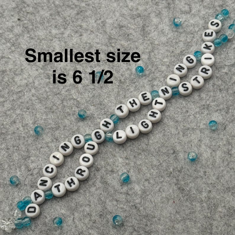 A handmade bracelet with white letter beads spelling "DANCING THROUGH THE LIGHT STRIKES". The smallest size is 6 1/2 inches. The bracelet is strung with clear and blue beads.