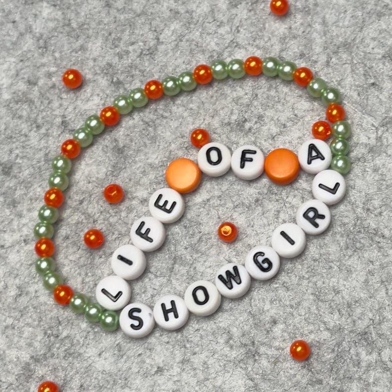 Bracelet made of 4mm dia light green and orange beads with white beads with black letters that say "LIFE OF A SHOWGIRL"