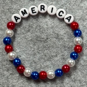 A patriotic bracelet with the word "AMERICA" spelled out in white letter beads. The bracelet features alternating red, white, and blue beads, creating a festive and colorful accessory.