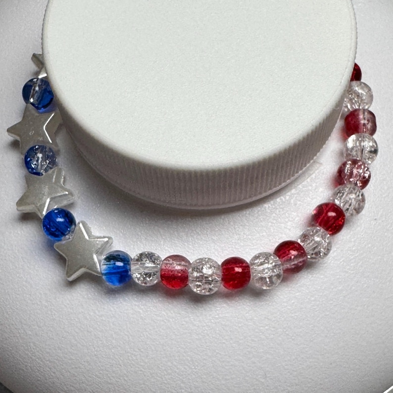 1 bracelet made from 4mm cracked glass beads that are red, clear white, and blue with 4 acrylic white stars.