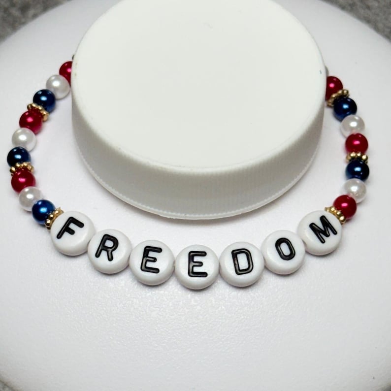 A patriotic bracelet with the word "FREEDOM" spelled out in white letter beads. The bracelet features red, white, and blue beads, creating a festive and colorful accessory. The bracelet is a stretch style.