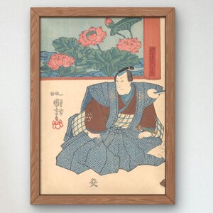 Peut inclure: Une estampe japonaise en bois encadrée représentant un homme en vêtements traditionnels assis avec un éventail à la main. L'estampe présente un fond de fleurs de lotus roses et de feuilles vertes.