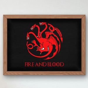 Peut inclure: Une impression encadrée avec un fond noir représentant un dragon rouge à trois têtes avec les mots "Fire and Blood" imprimés en dessous.