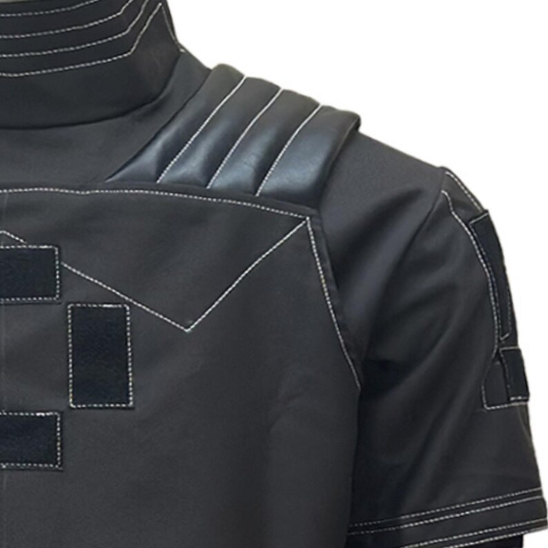May include: Black short-sleeved garment with white stitching details. Features a high collar and padded shoulder accents. Includes rectangular patches with velcro closures. The design is modern and sleek.