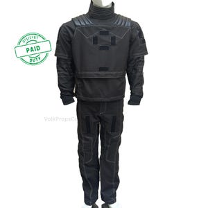 May include: Black tactical jumpsuit with white stitching, featuring a high collar, shoulder padding, and multiple patch details. The outfit includes a jacket and matching pants, designed for a functional and utilitarian aesthetic.